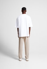 White oversized t-shirt with short sleeves, plain design. Paired with beige loose-fit pants and white sneakers, viewed from the back.