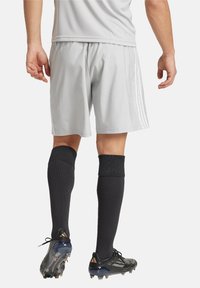 Grijze sportieve shorts met zijstrepen, gecombineerd met zwarte knielange sokken en zwarte voetbalschoenen. Focus op functioneel sportkledingontwerp.