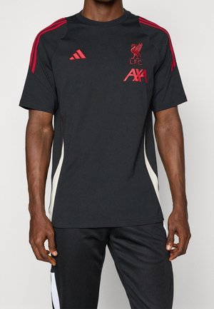 Homme portant un maillot d'entraînement noir du Liverpool FC avec des logos rouges et des bandes rouges sur les épaules, associé à un pantalon noir avec des détails blancs.