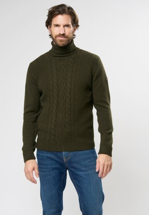 Suéter verde de punto con cuello vuelto, que presenta un patrón texturizado y puños acanalados. Se lleva con vaqueros azules para un look casual.