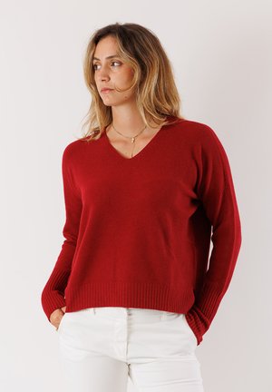 Maglione rosso a scollatura a V con maniche lunghe e orlo a coste. Realizzato in materiale morbido, presenta una vestibilità rilassata e una trama a maglia fine. Abbinato a pantaloni bianchi.