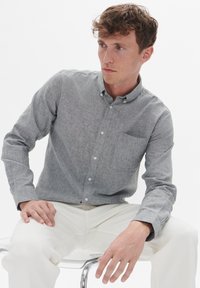 Grijze overhemd in een lichtgewicht stof, voorzien van een kraag, een enkele borstzak en lange mouwen, gecombineerd met een witte broek.
