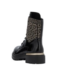 Bottines en cuir verni noir avec un revers tricoté doré et noir à motifs. Elles possèdent une semelle épaisse et un accent doré sur le talon.