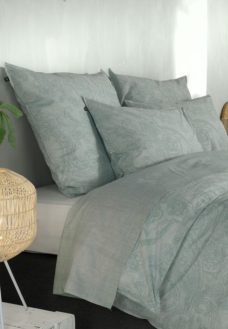 Juego de cama verde claro con patrones de paisley; incluye dos almohadas grandes y dos más pequeñas, visible tejido texturizado y elementos de diseño minimalistas.