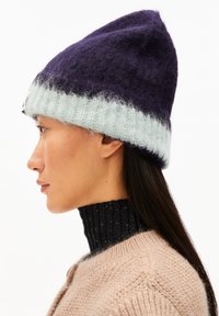 Paarse en lichtblauwe gebreide beanie met een zachte textuur en een puntige top, gedragen met een zwart geribbeld coltrui.