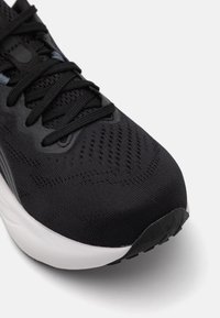 Black athletic shoe with a textile upper featuring textured surface, reinforced toe, and contrasting white sole. Laces are black.