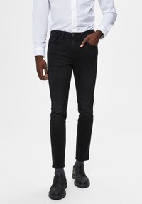 Svarta denimjeans med slim fit, framfickor och knappstängning. Bärs med en vit skjorta och svarta skor.