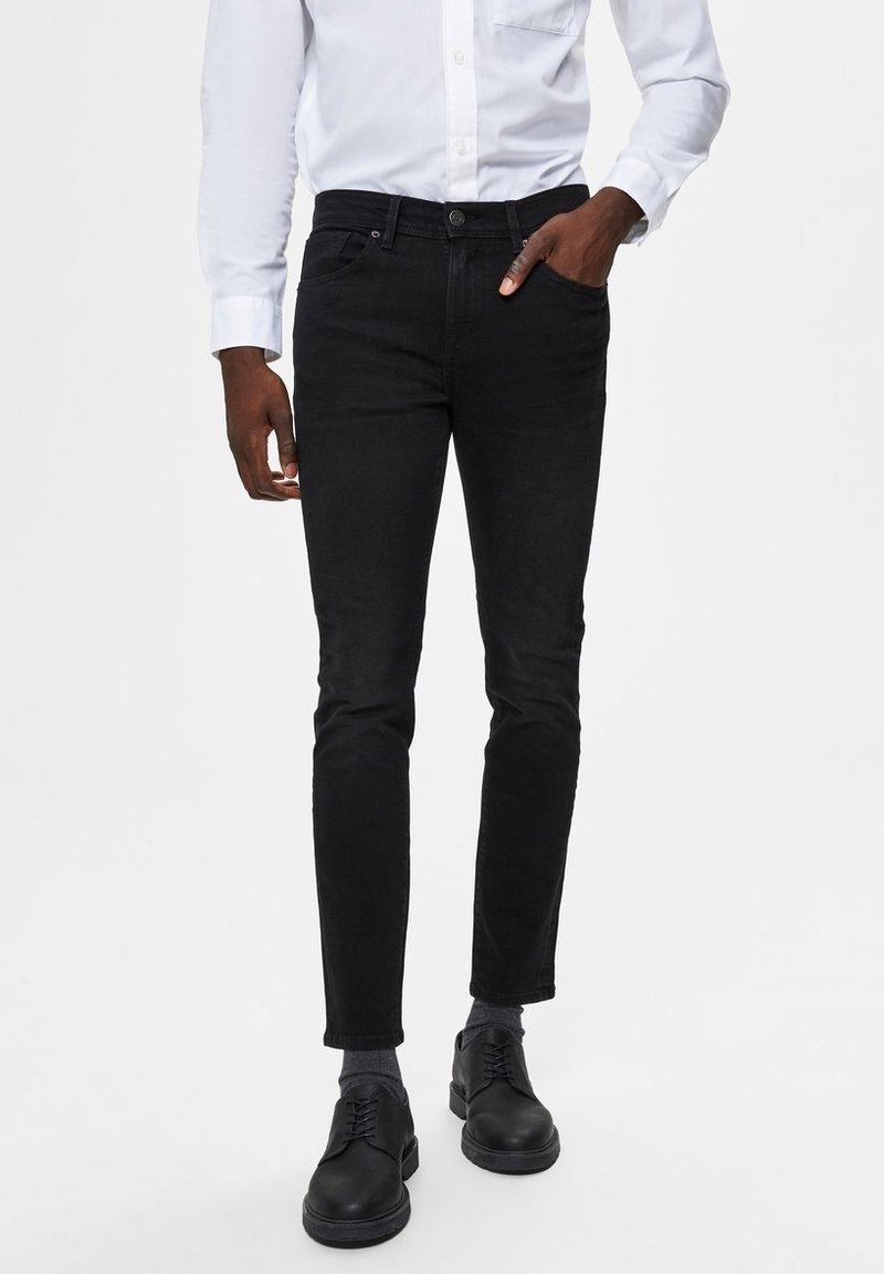 Svarta denimjeans med slim fit, framfickor och knappstängning. Bärs med en vit skjorta och svarta skor.