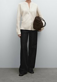 Lys cremet langærmet skjorte med knapper og mandarinkrave, parret med mørke brede jeans og en brun ruskinds skuldertaske.