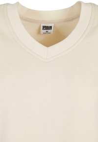 Pull col en V couleur crème avec col côtelé et étiquette Urban Classics taille XS cousue à l'intérieur de l'encolure.