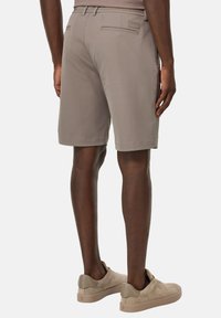Bermuda beige con una vestibilità sartoriale, caratterizzate da una frontale liscia, due tasche posteriori e una texture morbida. Abbinati a scarpe slip-on di un beige chiaro.