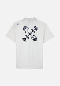T-shirt en coton blanc avec un motif floral bleu foncé au dos, manches courtes et encolure ronde. Comprend une petite étiquette de marque.