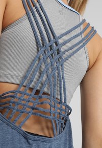 Grå ribbad sporttop med korsade blå remmar på baksidan som skapar en öppen design. Slät textur med en åtsittande form.