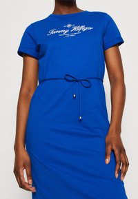 Robe T-shirt en coton bleu avec un col rond, des manches courtes et une taille à cordon. Présente un logo imprimé blanc sur la poitrine.