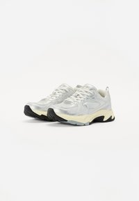 Witte sportieve schoenen van reflecterend synthetisch materiaal, met een gestructureerd ontwerp, een zwarte rubberen zool en een lichtgekleurde tussenzool. Platte veters.