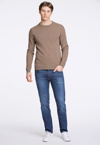 Brun stickad tröja med rund hals, tillsammans med mörkblå jeans och vita sneakers. Outfiten har en avslappnad, figurnära design.