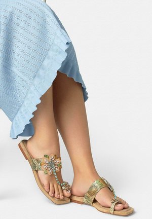 Feet wearing gold textured sandals with flower and turquoise bead embellishments, paired with a light blue ruffled skirt.