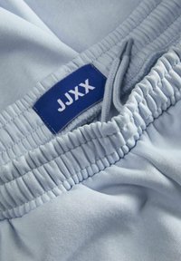 Shorts en tissu bleu clair avec une taille élastique, un cordon de serrage et une étiquette portant le texte "JJXX" en blanc sur un fond bleu.