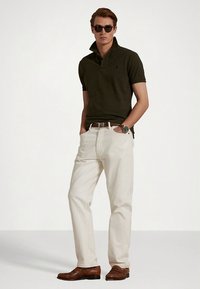 Πράσινο σκουρόχρωμο πόλο μπλουζάκι με κοντά μανίκια και γιακά, σε συνδυασμό με ανοιχτό μπεζ παντελόνι και καφέ δερμάτινα παπούτσια. Περιλαμβάνει γυαλιά ηλίου και ρολόι.