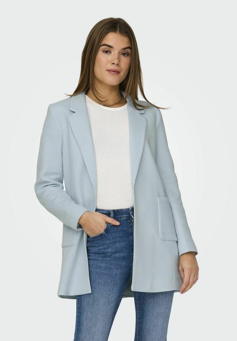 Sacou de un albastru deschis, realizat dintr-un material texturat, cu guler clasic, deschis în față și buzunare frontale, purtat peste un top alb și blugi.