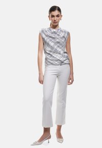 Weißes ärmelloses Top mit einem blauen Karomuster, kombiniert mit weißen, enganliegenden Hosen und cremefarbenen spitzen High Heels. Glatte Textur überall.
