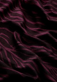 Schwarzer Stoff mit dunkelvioletten, zebraartigen Streifen, gezeigt mit Falten und strukturiertem Gewebemuster.