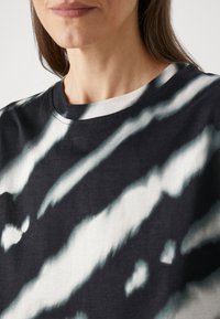 Camiseta de tie-dye en blanco y negro con cuello redondo, textura suave y patrones abstractos de rayas y manchas.