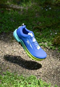 Baskets de course bleues avec une tige texturée, accents blancs et vert fluo, conception légère et semelle rembourrée visible, suspendues dans les airs.