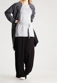 Pullover grigio con cintura su pantaloni neri a gamba larga, abbinato a un cardigan a righe nere. Tessuto casual e leggero, vestibilità rilassata.