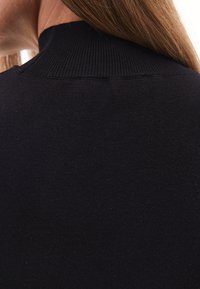 Prenda de punto negra con canalé que presenta un cuello alto. Textura suave con detalles sutiles en la costura del cuello.