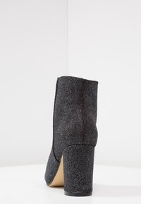 Svart texturerad ankelsko med hög klack, med en slät yta och en avsmalnande siluett, designad för en åtsittande passform runt vristen.