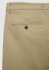 Pantaloni beige con una tasca posteriore dotata di chiusura a bottone nero. Il tessuto ha una superficie liscia con un classico motivo tessuto.