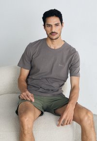 Sivý bavlnený tričko s krátkymi rukávmi a okrúhlym výstrihom, s malým logom "BOSS" na hrudi, v kombinácii so zelenými šortkami.