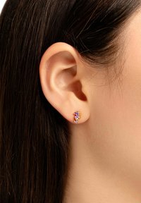 Guldtonade örhängen med flerfärgade ädelstenar i en böjd design, bärs i örsnibben, med jämn hud och mörkt hår i fokus.