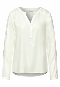 Blusa bianca a maniche lunghe con scollatura a V e pattina con bottoni. Realizzata in un tessuto morbido, presenta un orlo leggermente curvo e spalle arricciate.