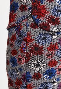 Geweven stof met rood, blauw en wit bloemmotief op een grijze achtergrond met een gestructureerde afwerking en subtiele ruitjes.