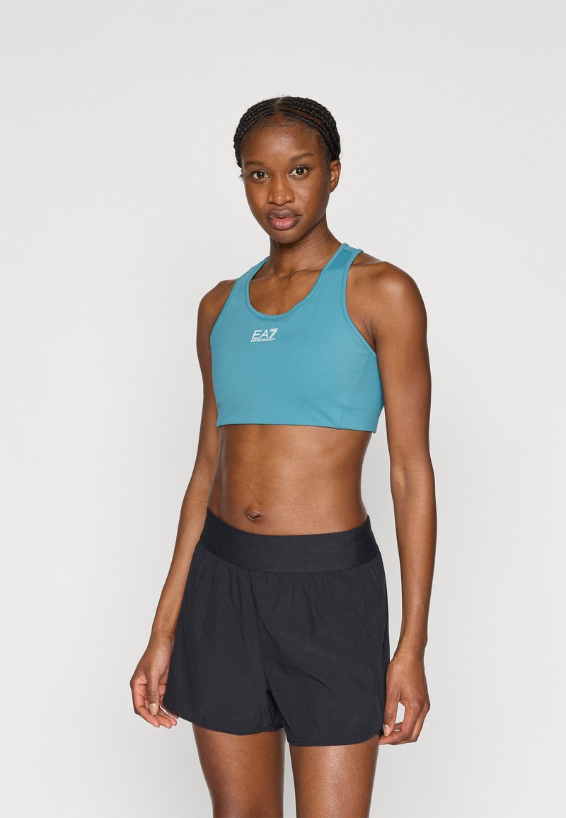 Τζίντζερ σπορ μπουστάκι με στρογγυλή λαιμόκοψη και λογότυπο στο κέντρο· συνδυασμένο με μαύρο σορτς ψηλής μέσης. Λείο ύφασμα με εφαρμοστή σχεδίαση.