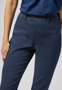 Dunkelblaue Denim-Hosen mit einer glatten Textur, schmaler Passform und elastischem Bund. Verfügt über standardmäßige Fronttaschen und dezente Nähdetails.