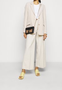 Light beige oversized blazer, white t-shirt, cream wide-leg pants, yellow slide sandals, and a black crossbody bag with a patterned detail.