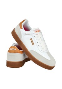 Zapatillas casuales blancas y beige con suelas marrones, cordones y la marca "Joma" en los laterales y el talón, colocadas sobre un fondo blanco.
