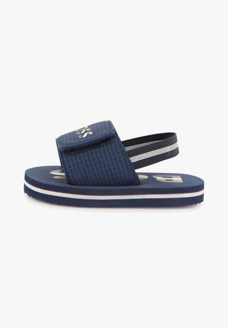 Sandale pour enfants bleu marine avec bride avant réglable et bride de talon élastique noire, rayures blanches et brunes sur le bord de la semelle.