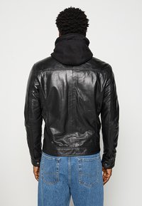 Schwarze Lederjacke mit einer körperbetonten Passform, hochschließendem Kragen, Nahtdetails und einer Kapuzen-Sweatshirt-Schicht darunter.