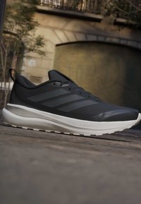 Black and gray running shoe with white cushioned sole resting on stone pavement in an outdoor urban setting.