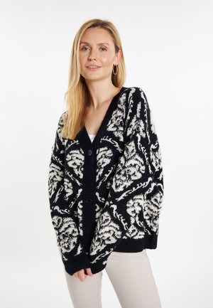 Schwarz-weißer gemusterter Cardigan mit V-Ausschnitt, Knopfverschluss und weit geschnittenen Ärmeln, aus strukturiertem Strickstoff.