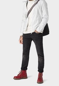 Lekka, biała kurtka zapinana na zamek, kremowy sweter, czarne spodnie slim fit i czerwone skórzane botki z detalami w postaci sznurówek. Czarna torba na ramię.