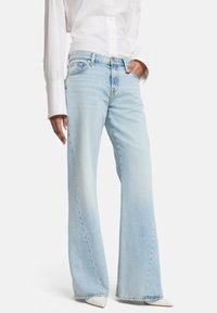 Jean en denim bleu clair avec une taille mi-haute, un léger délavage et un design classique à cinq poches. Associé à une chemise blanche à boutons.