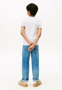 T-shirt bianco a maniche corte, jeans in denim blu, sneaker beige. La maglietta presenta un piccolo dettaglio rosso e blu sul colletto. Vestibilità classica.