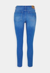 Vaqueros ajustados en denim azul medio con un efecto desgastado, que cuentan con dos bolsillos traseros y una etiqueta de cuero marrón en la cintura.
