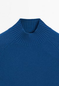 Modrý pletený svetr se širokým, žebrovaným stojáčkovým límcem a raglánovými rukávy, položený na bílém pozadí.