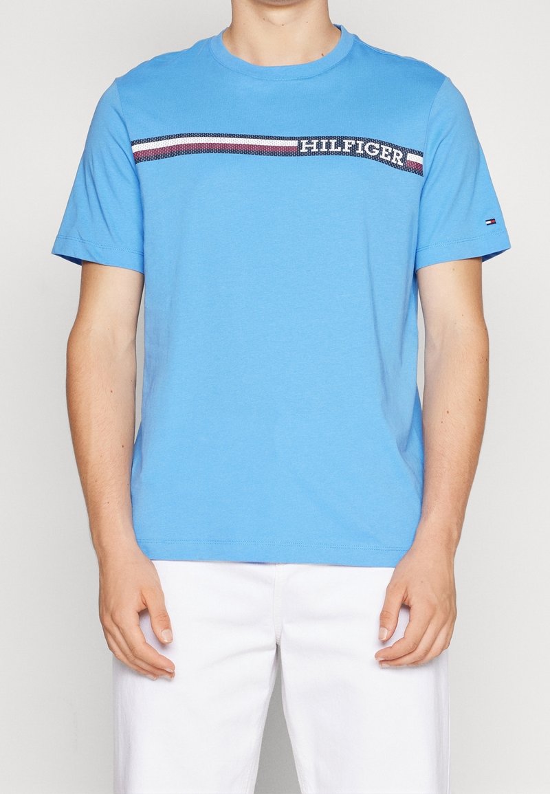 Blue cotton t-shirt with a crew neck, featuring a horizontal striped design in red, white, and navy, and the word "HILFIGER" in black.